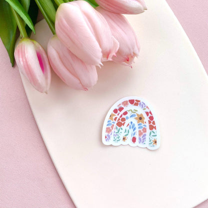 Colourful rainbow sticker with floral pattern against a cream background with pink tulips.