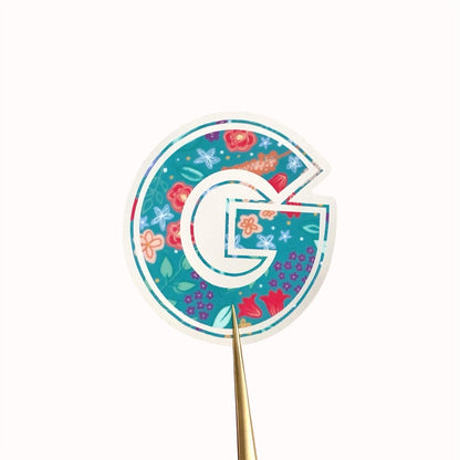Decorative letter 'G' sticker with floral pattern on a white background