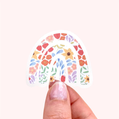 Hand holding a rainbow sticker with a  colourful floral design on a white background