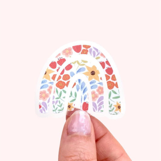 Hand holding a rainbow sticker with a  colourful floral design on a white background