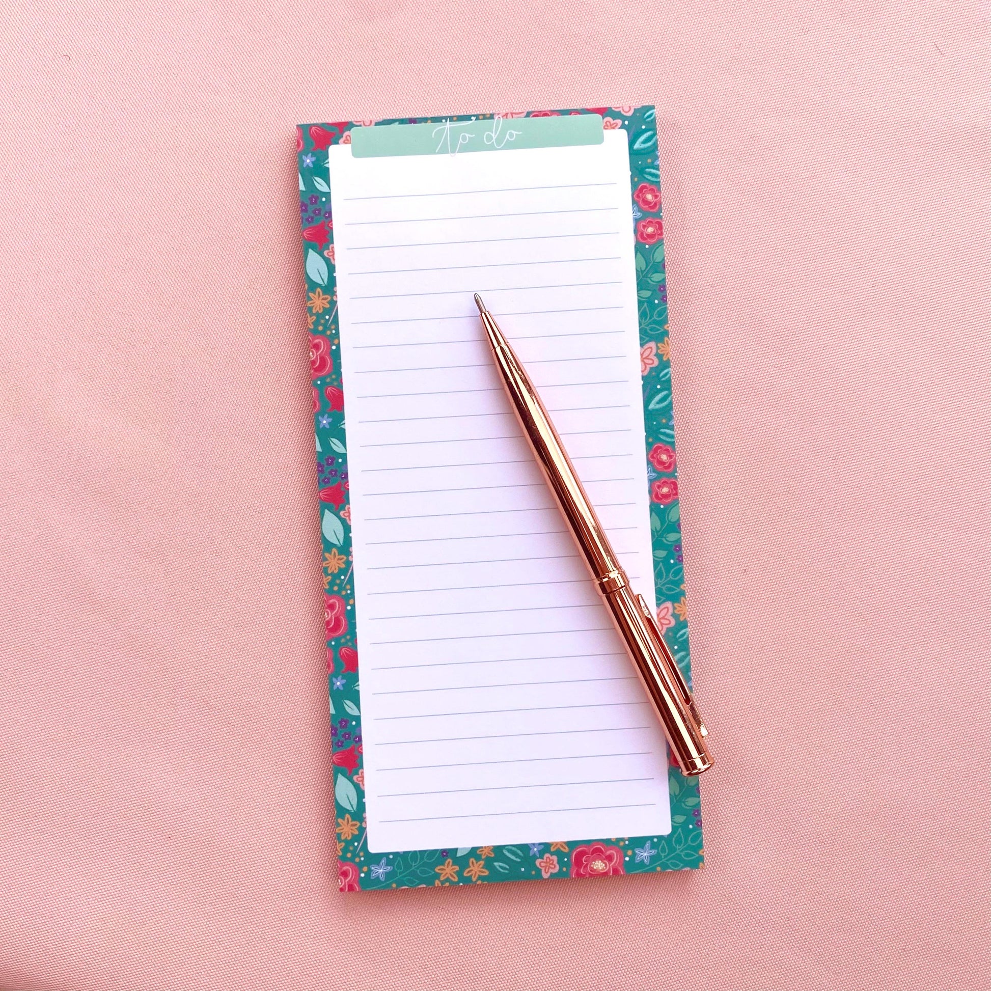 Floral notepad with a pen on a pink background