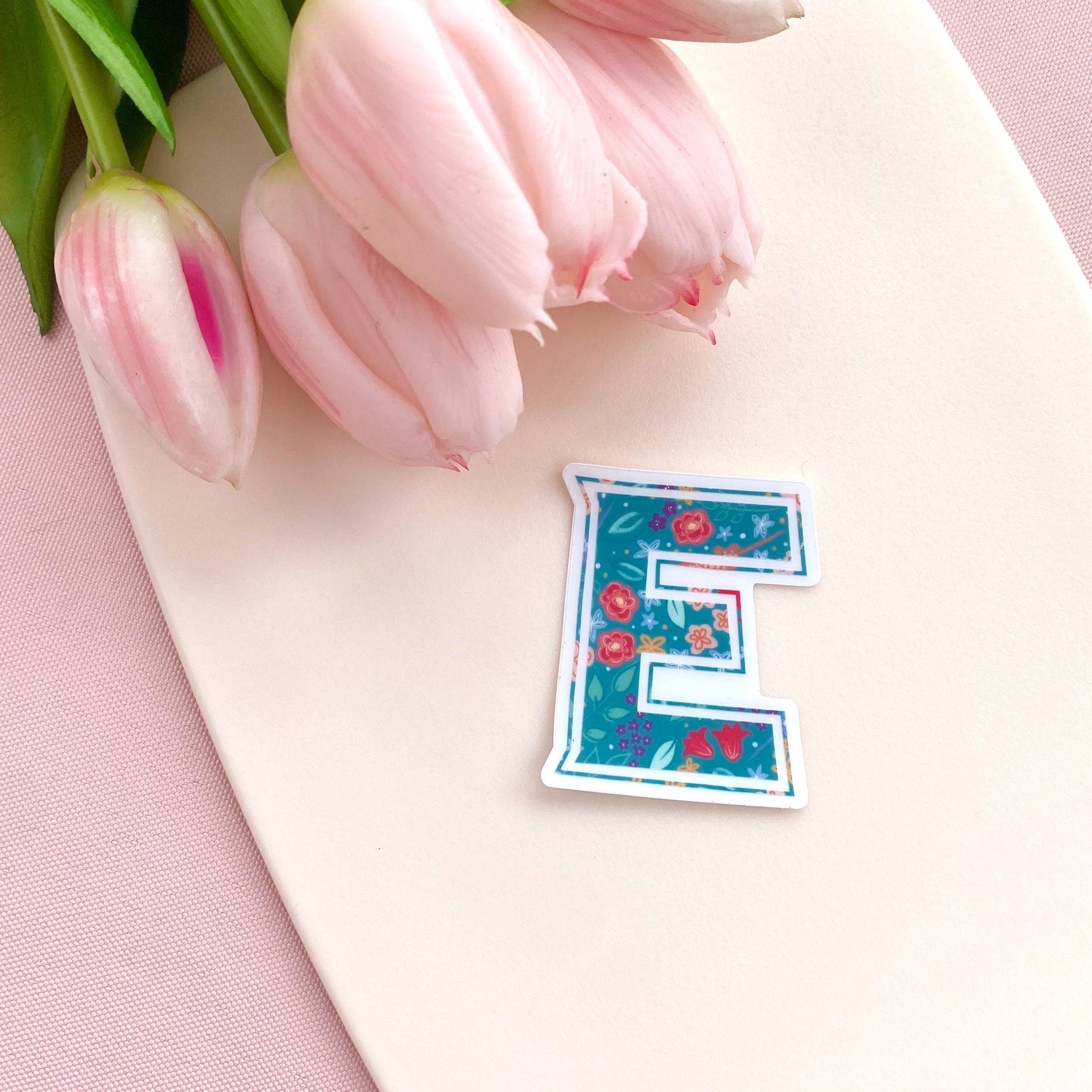 Floral letter 'E' sticker on a pink surface with pink tulips