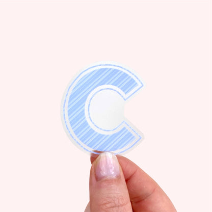 Hand holding a blue letter 'C' sticker against a white background