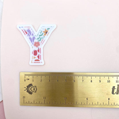 Floral letter 'Y' sticker next to a ruler on a pink background