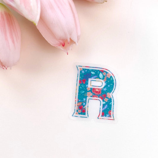 Floral letter 'R' sticker on a cream background with pink flowers.