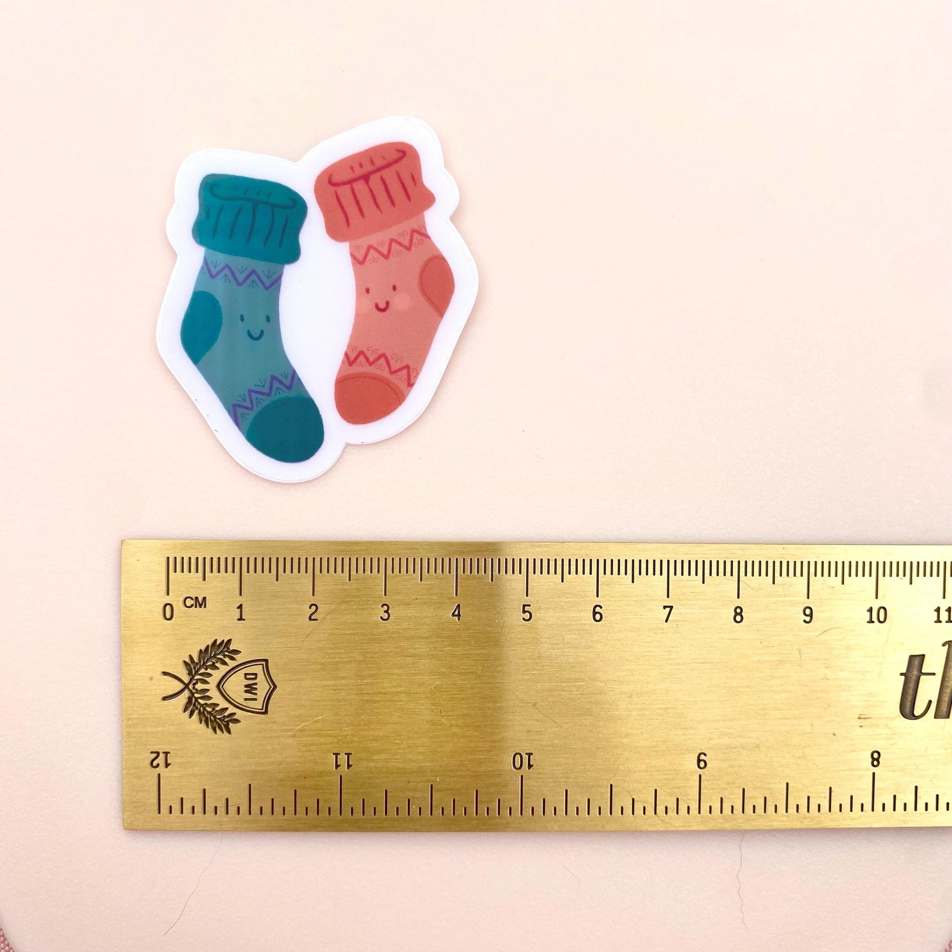 A sticker of two cartoon-style socks with smiling faces next to a ruler on a beige background