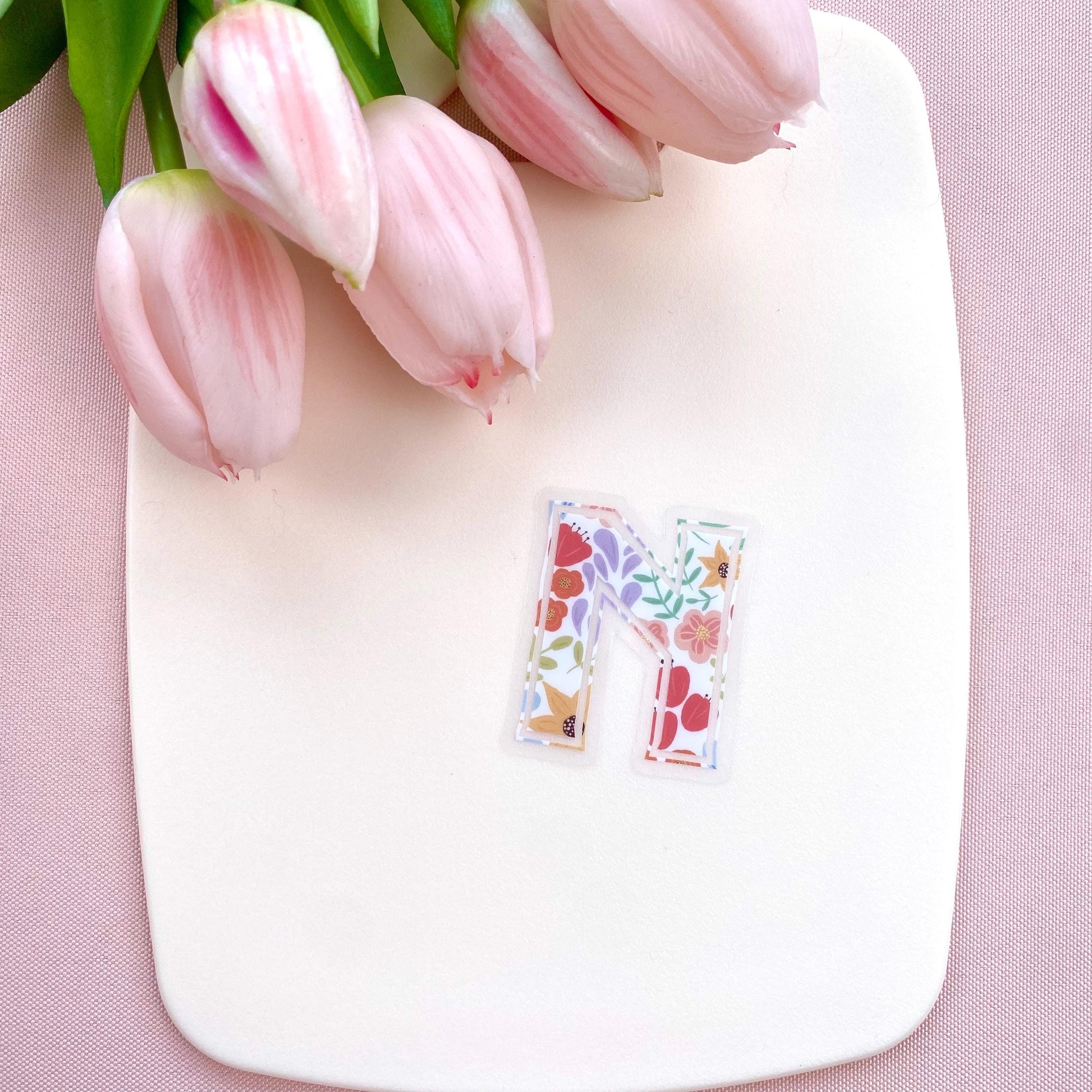Floral letter 'N' sticker on a white board with pink tulips on a pink background