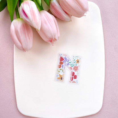 Floral letter 'N' sticker on a white board with pink tulips on a pink background