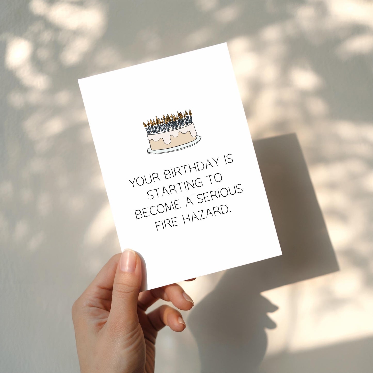 Hand holding a card with a birthday cake illustration and humorous text on a light background