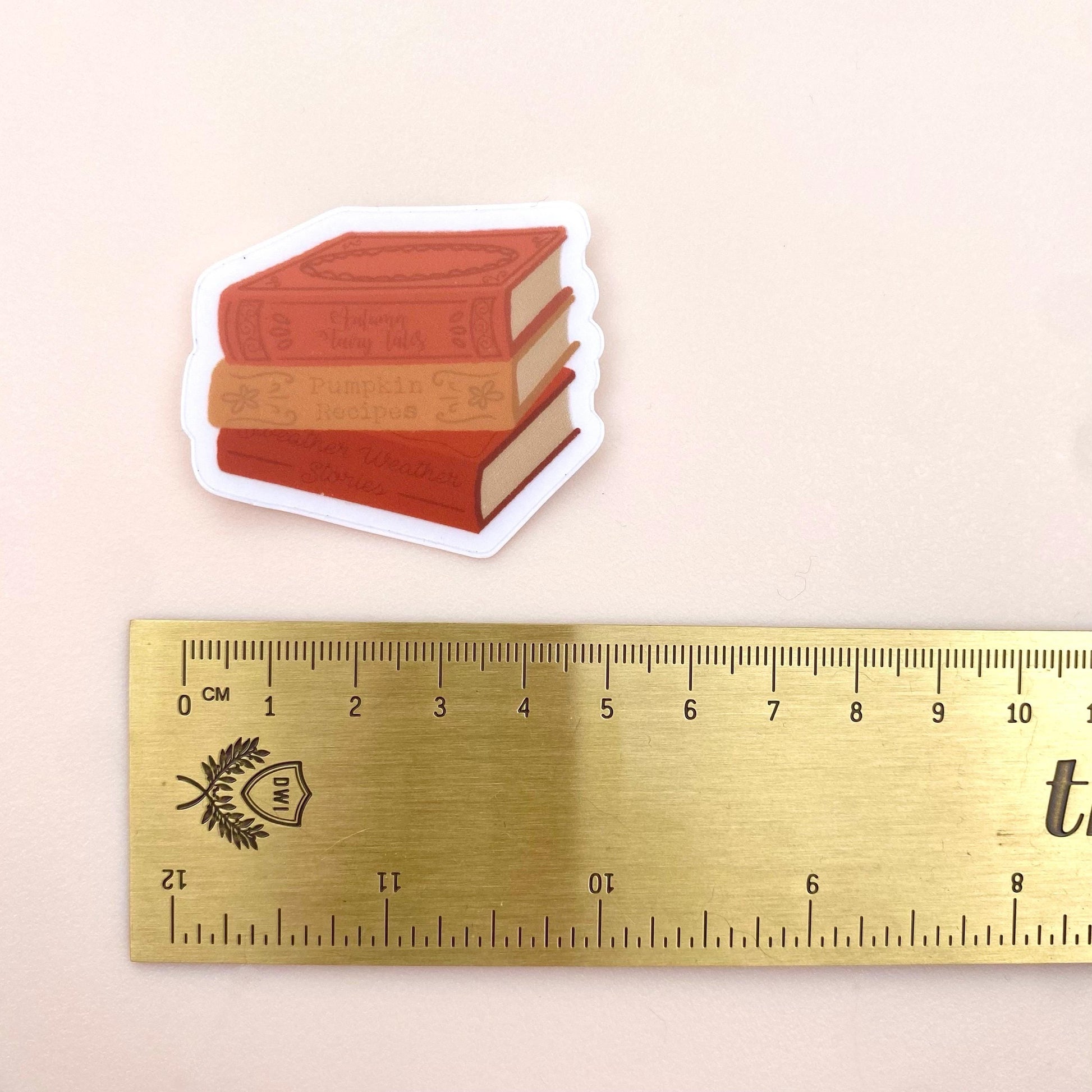 Sticker of stacked books next to a ruler on a beige background