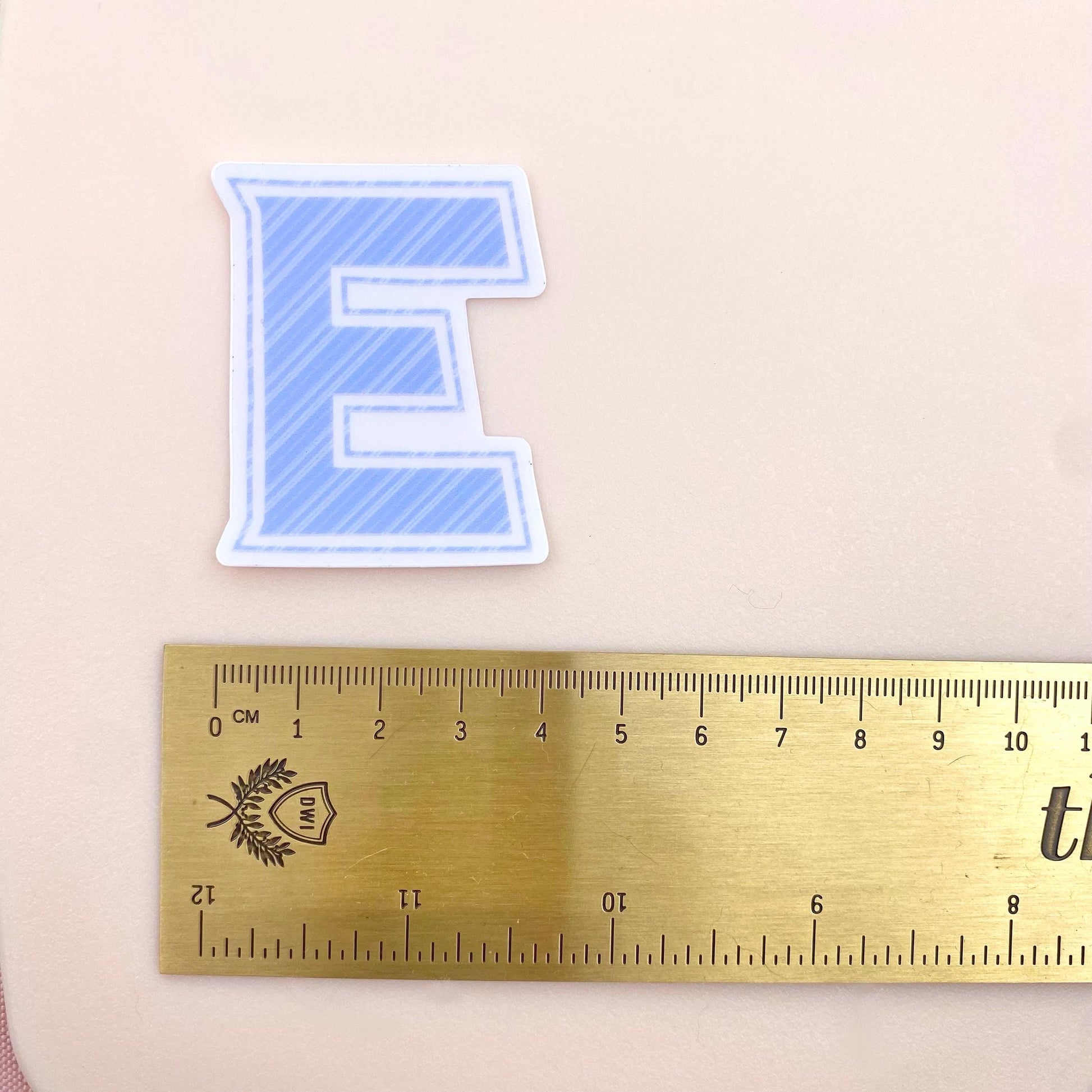 Blue striped letter 'E' sticker with a ruler for scale on a beige background