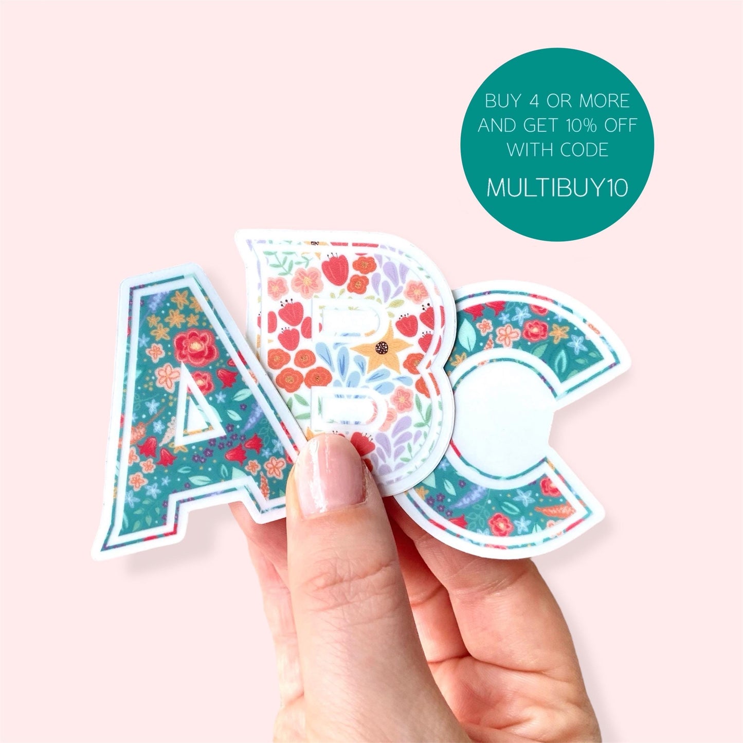 Hand holding floral-patterned letter stickers 'A', 'B' and 'C' on a pink background with promotional text.