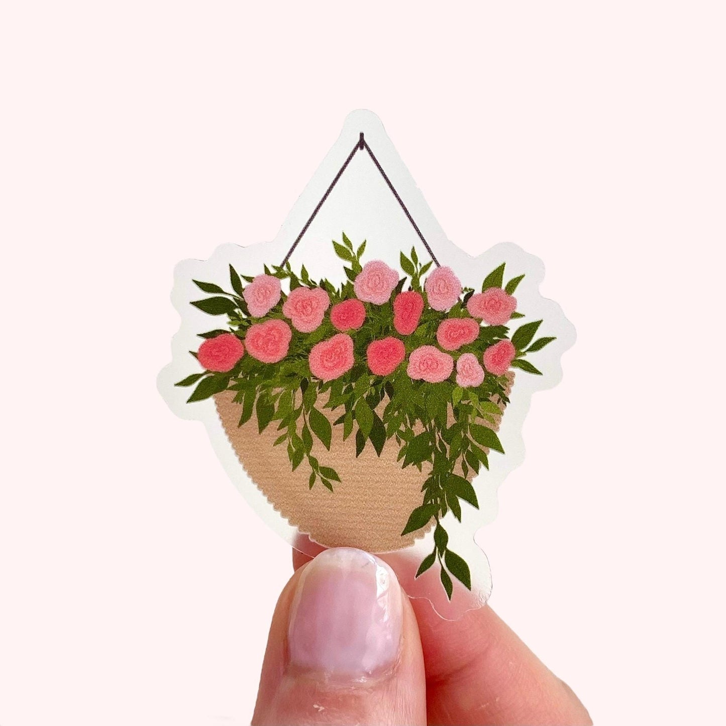 A sticker with a hanging planter with pink flowers held up by a hand against a white background.