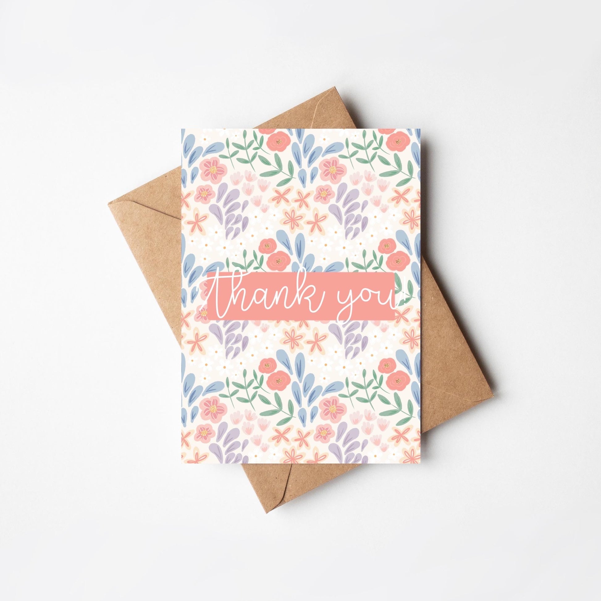 Greeting card with floral design and 'thank you' text, accompanied by a brown envelope on a white background.