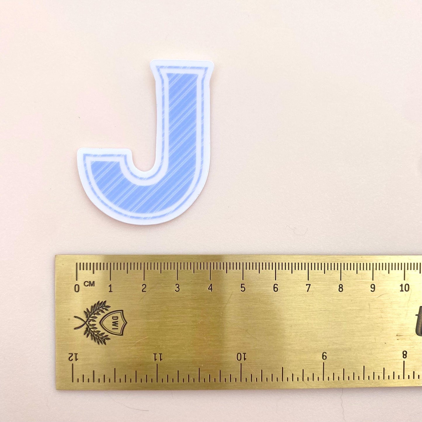 Letter 'J' sticker next to a ruler on a beige background
