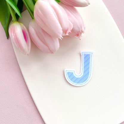 Pink tulips on a white board with a blue letter 'J' sticker on a pink background