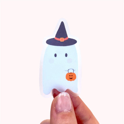 Halloween-themed ghost sticker with a witch hat and pumpkin held by a hand on a white background