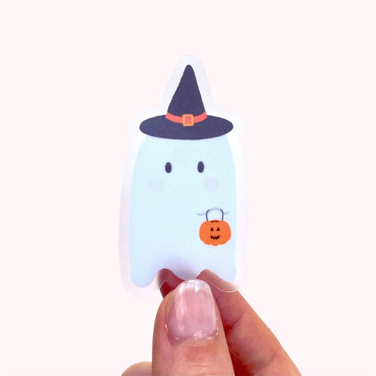Halloween-themed ghost sticker with a witch hat and pumpkin held by a hand on a white background