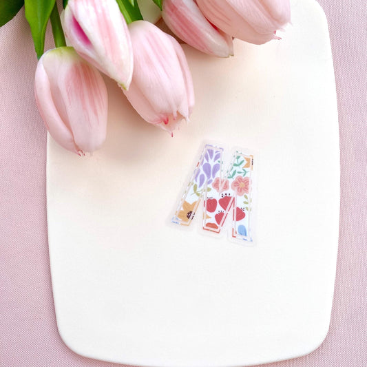 Decorative letter 'M' sticker with floral patterns on a white background with pink tulips