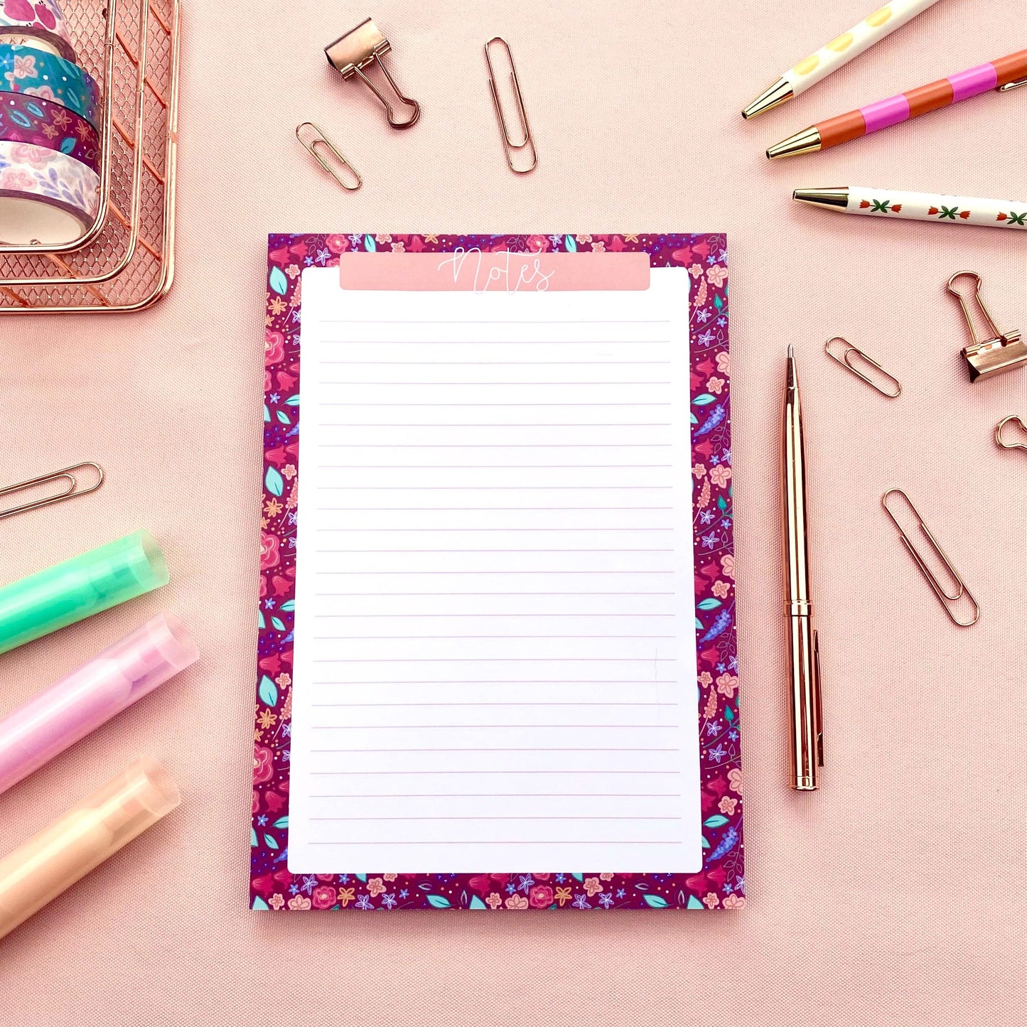 Floral notepad with stationery items on a pink background