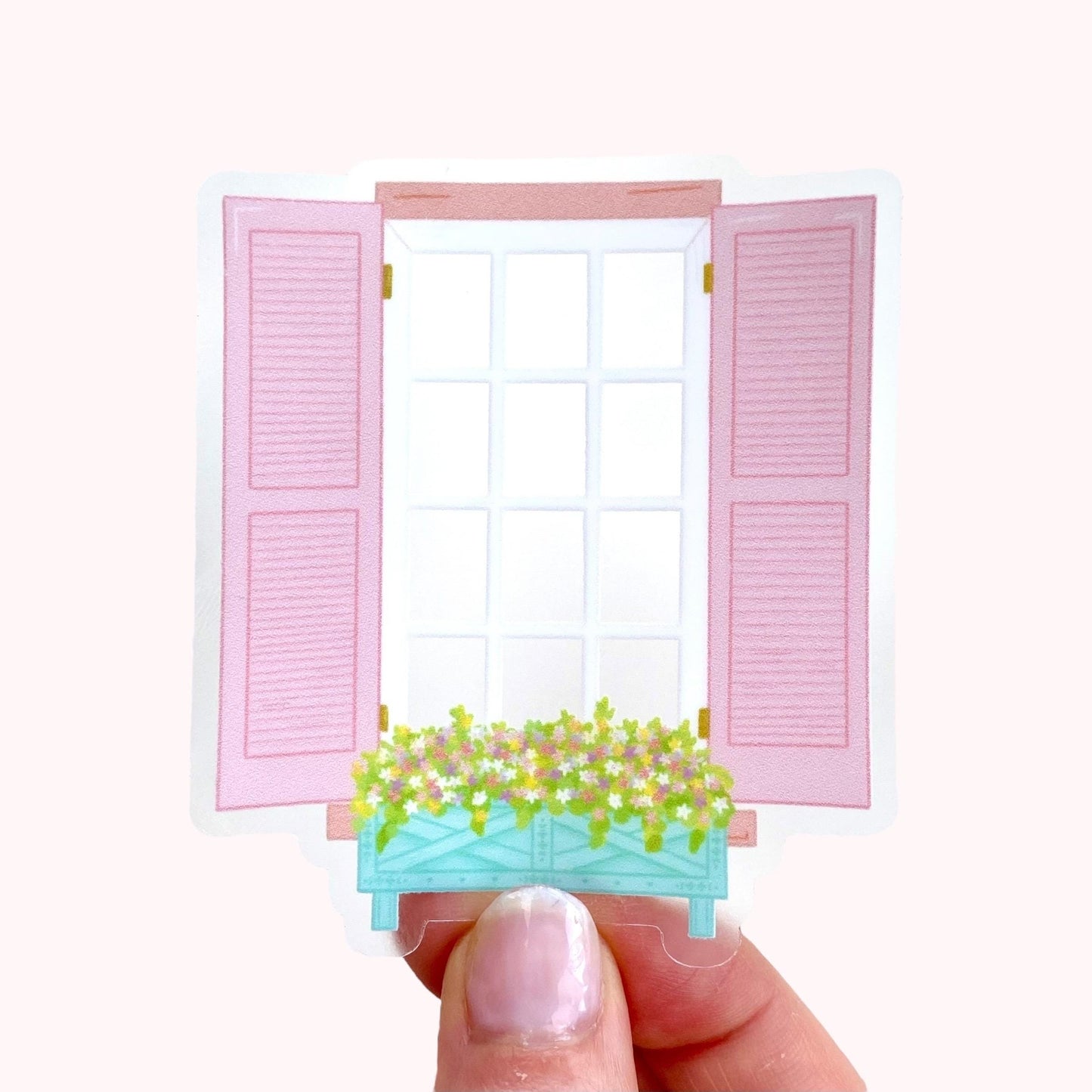 Transparent sticker of a window with pink shutters and a flower box held by a hand on a white background
