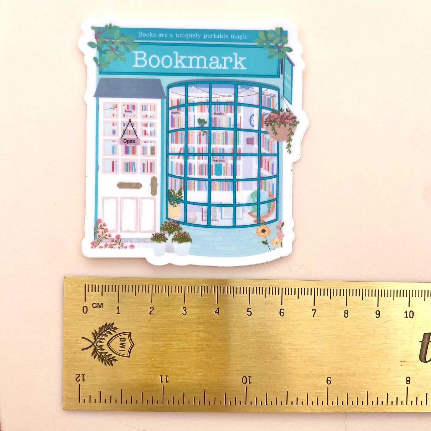 Teal Blue bookmark sticker with colourful books and flowers with a gold ruler for scale.