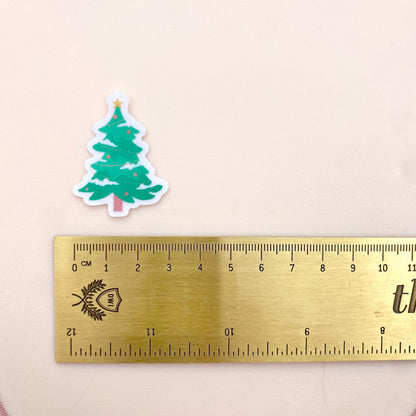 Green Christmas tree sticker next to a ruler on a beige background