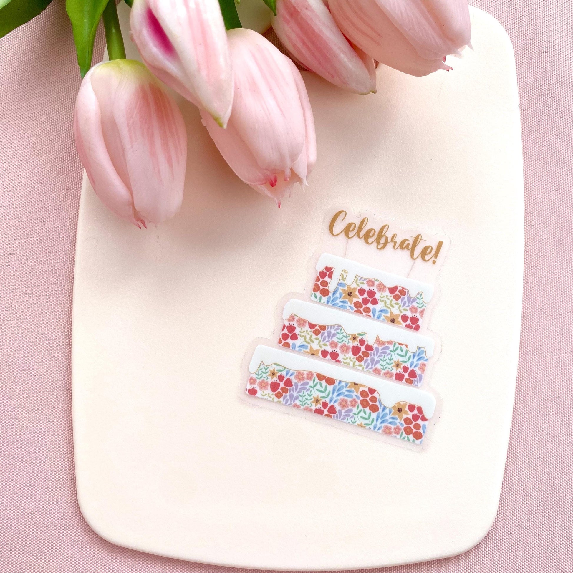 Decorative sticker with floral designs and 'Celebrate!' text on a pink background with tulips.