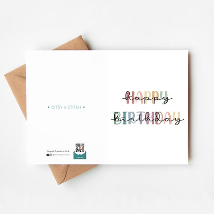 Birthday card with 'Happy Birthday' text in rainbow colours and a brown envelope on a white background