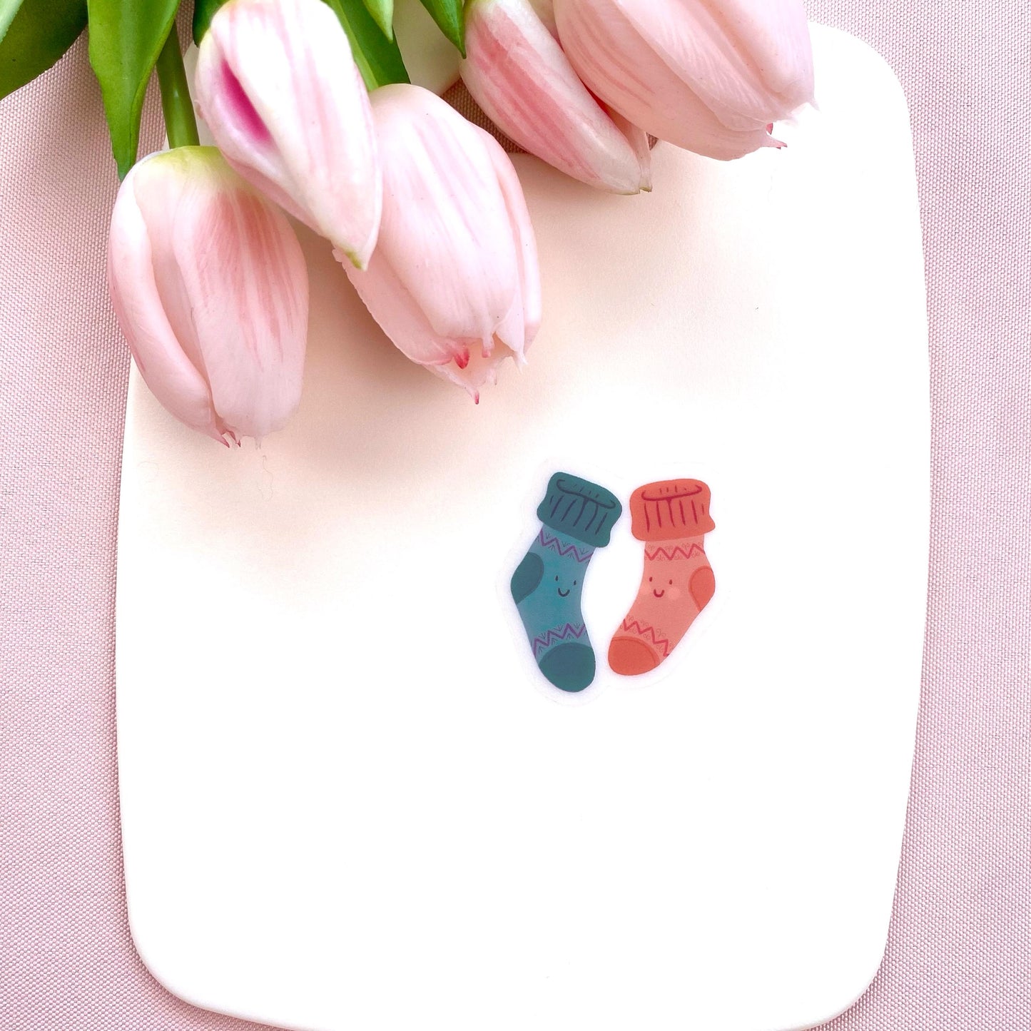 A sticker with two colourful socks with smiley faces on a white background with pink tulips