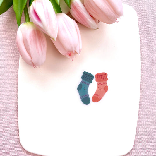 A sticker with two colourful socks with smiley faces on a white background with pink tulips