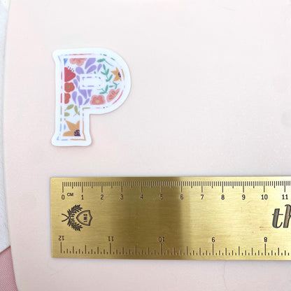 Floral letter 'P' sticker next to a ruler on a pink background