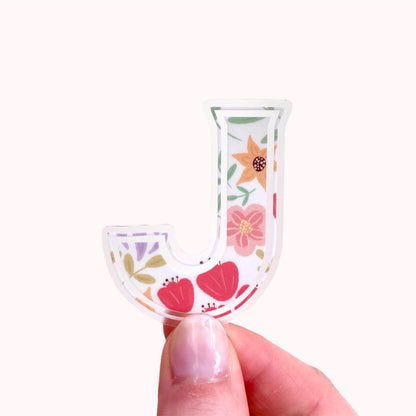 Floral-patterned letter 'J' sticker held by a hand on a white background