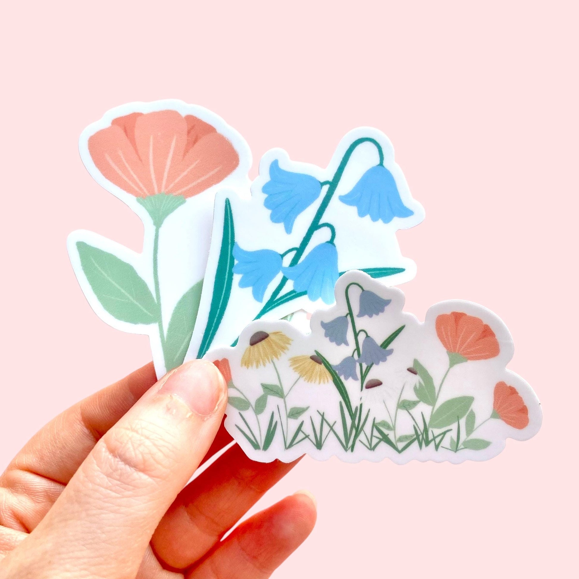 Hand holding floral stickers against a pink background