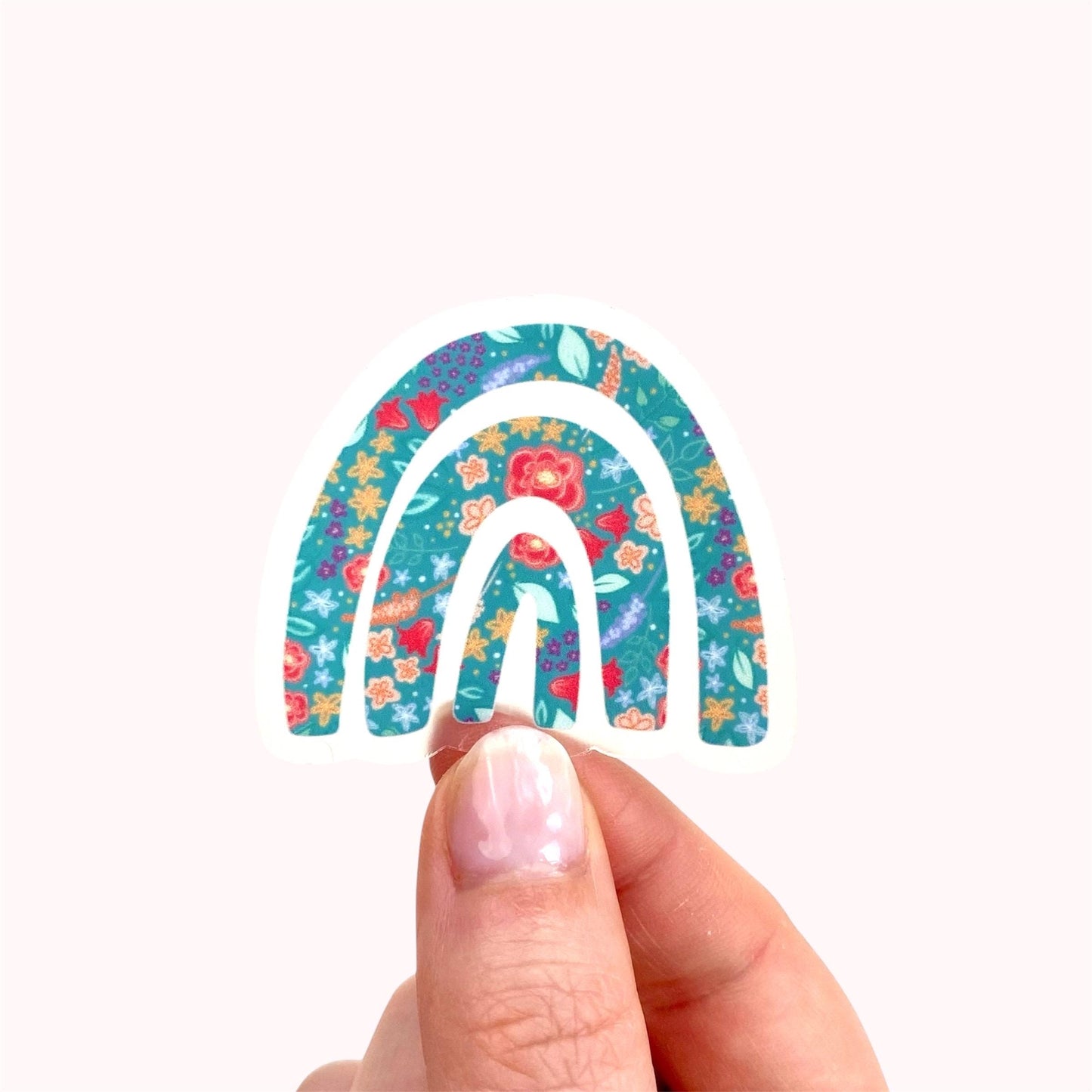Hand holding a decorative rainbow sticker with floral patterns on a white background