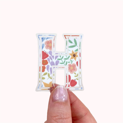 Letter 'H' sticker with floral design held by hand against a white background