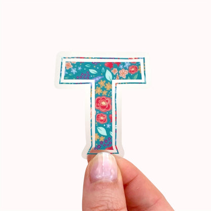 Floral letter 'T' sticker held by a hand on a white background