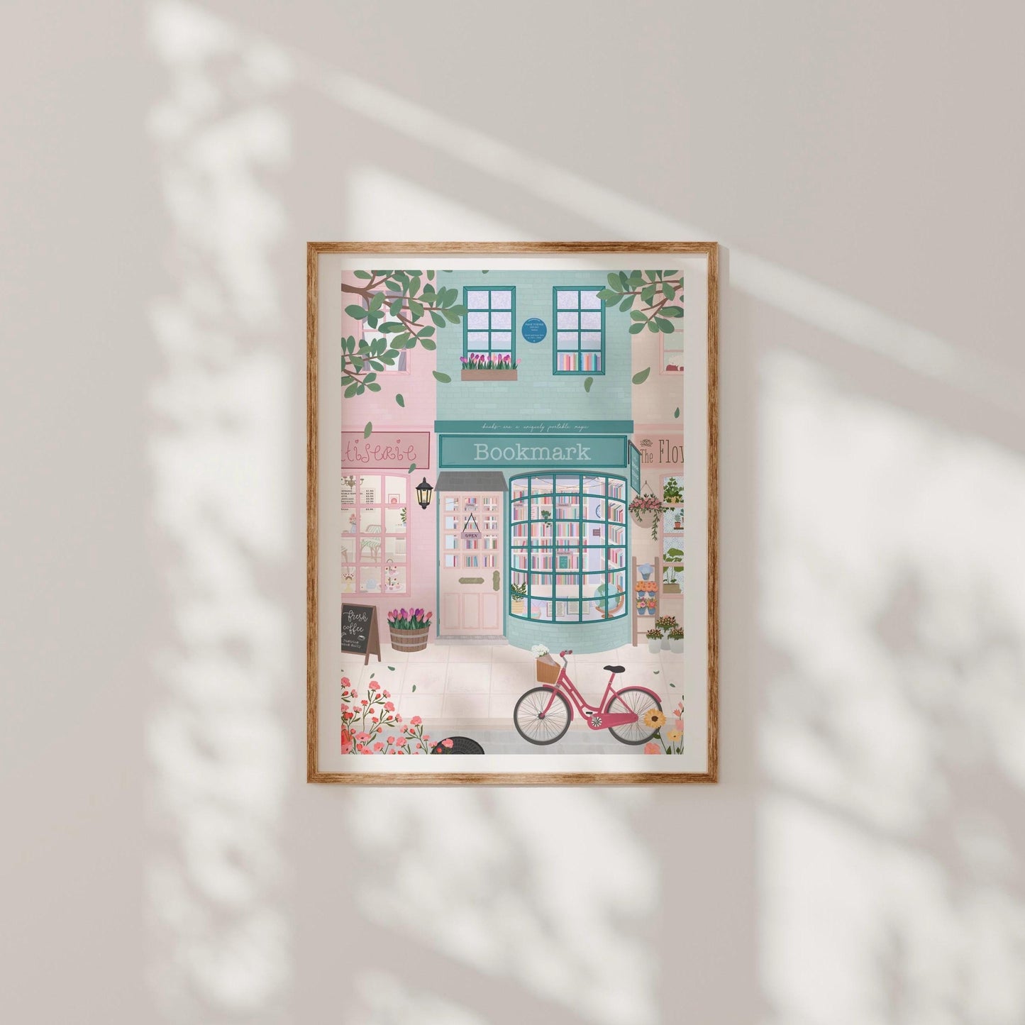 Framed illustration of a bookshop with a pink bicycle outside on a light grey wall.