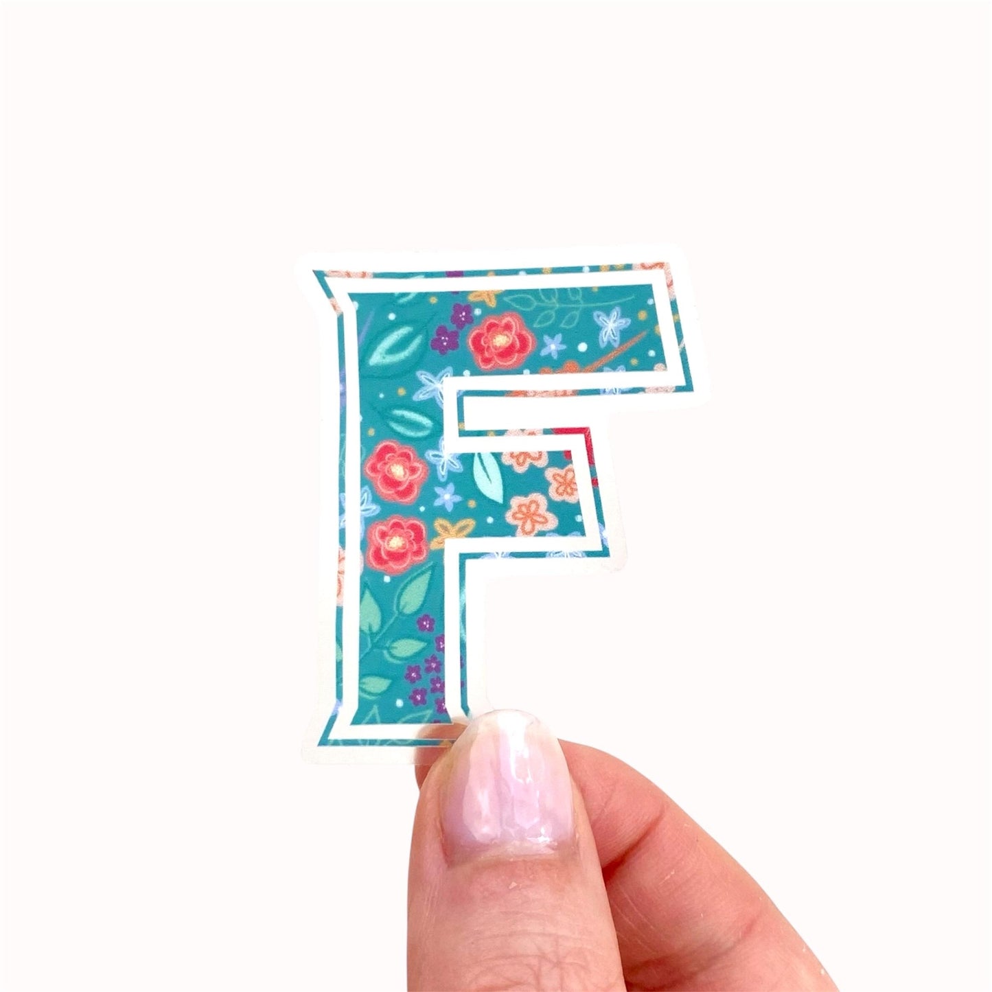 Floral-patterned letter 'F' sticker held by a hand on a white background