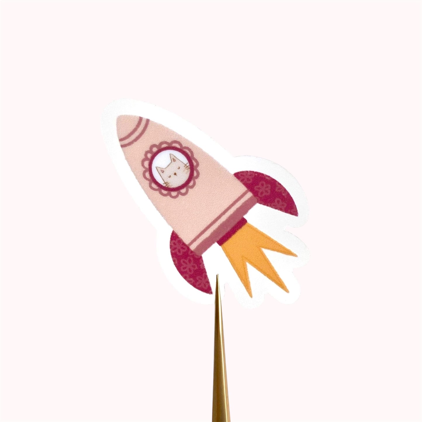 A pink rocket sticker with a grey cat in the window against a cream background