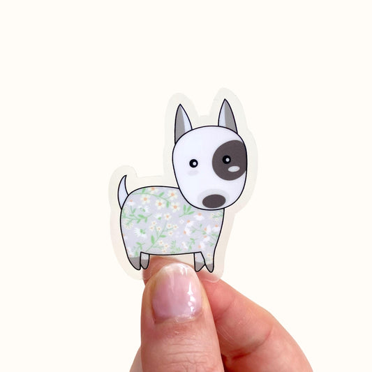 Hand holding a sticker of a cartoon dog with floral pattern on a white background