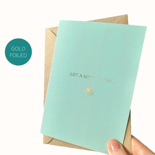 Mint blue card with gold text and daisy design, held by a hand on a white background.