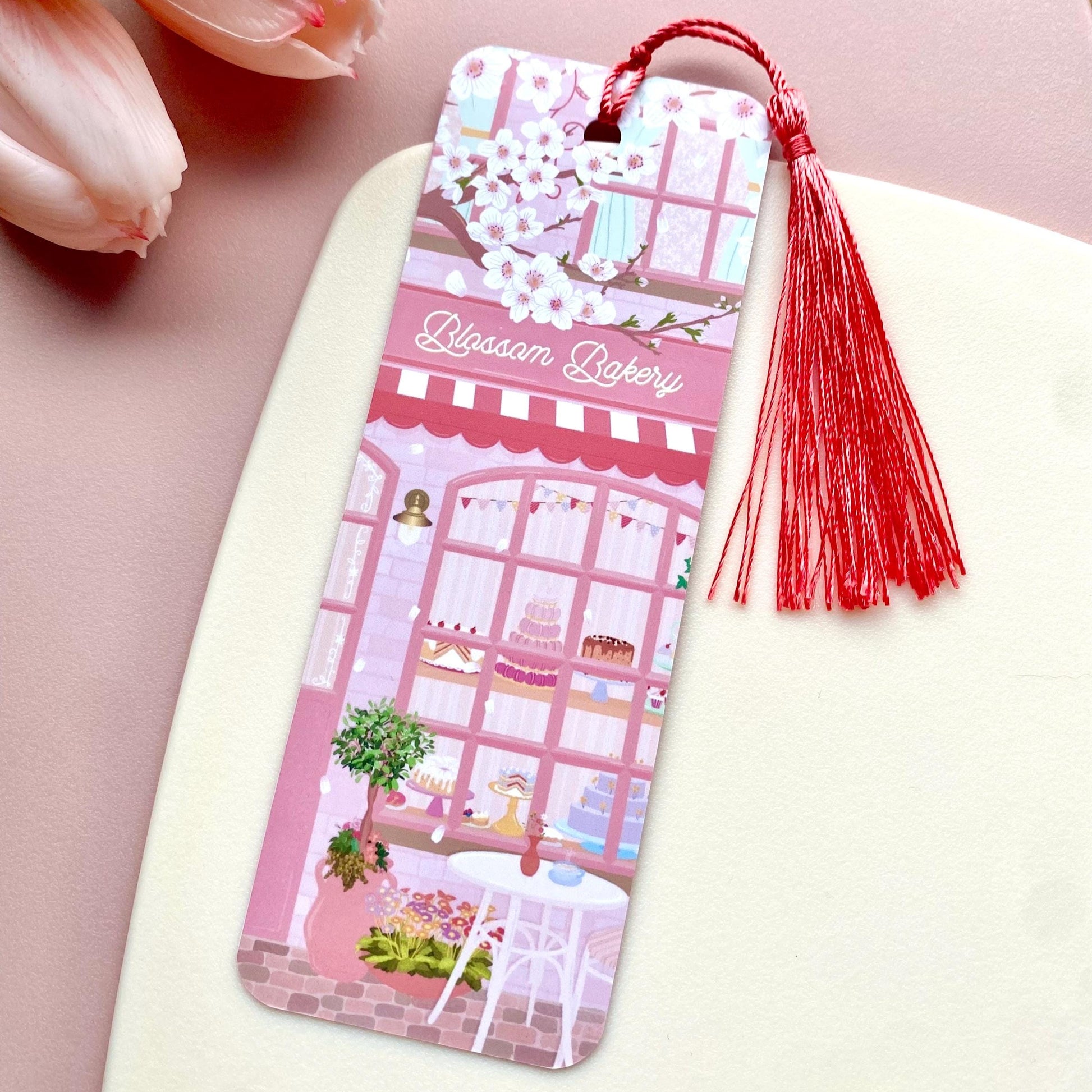 Bookmark with a bakery design and pink tassel on a pink surface with tulips.