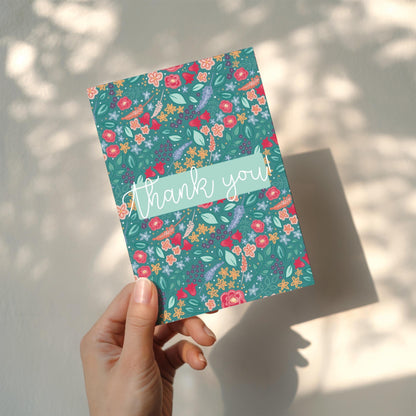 Floral patterned card with 'thank you' text held by a hand against a light background