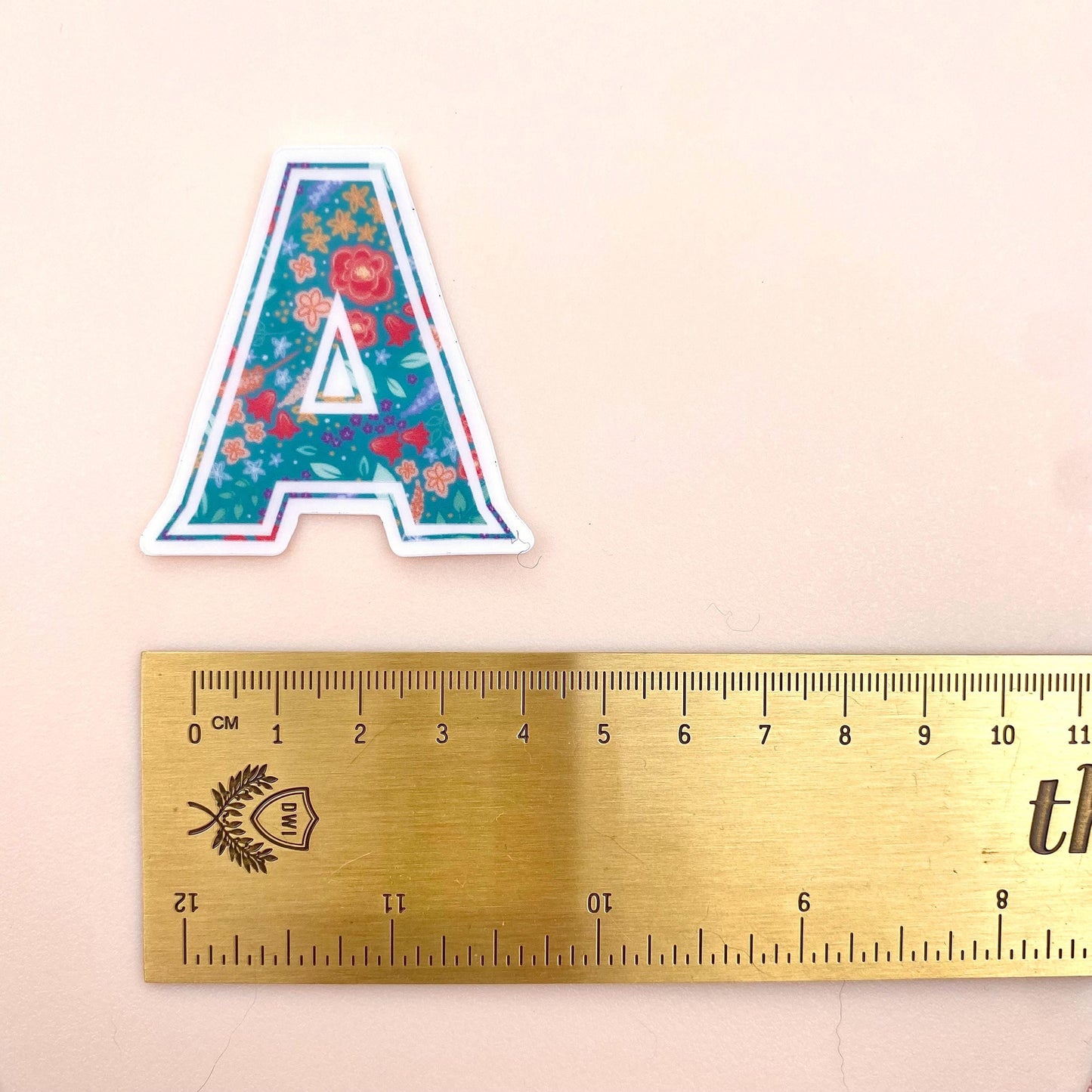 Floral letter 'A' sticker next to a ruler on a beige background