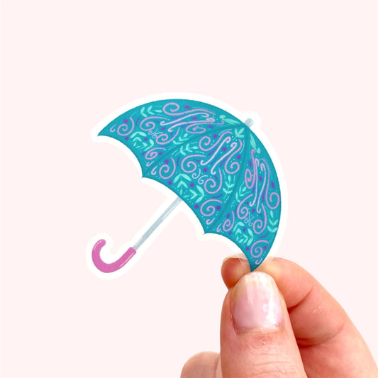 Hand holding a decorative turquoise umbrella sticker with pink handle on a white background