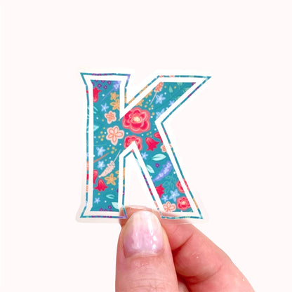 Colorful letter 'K' sticker held by a hand on a white background