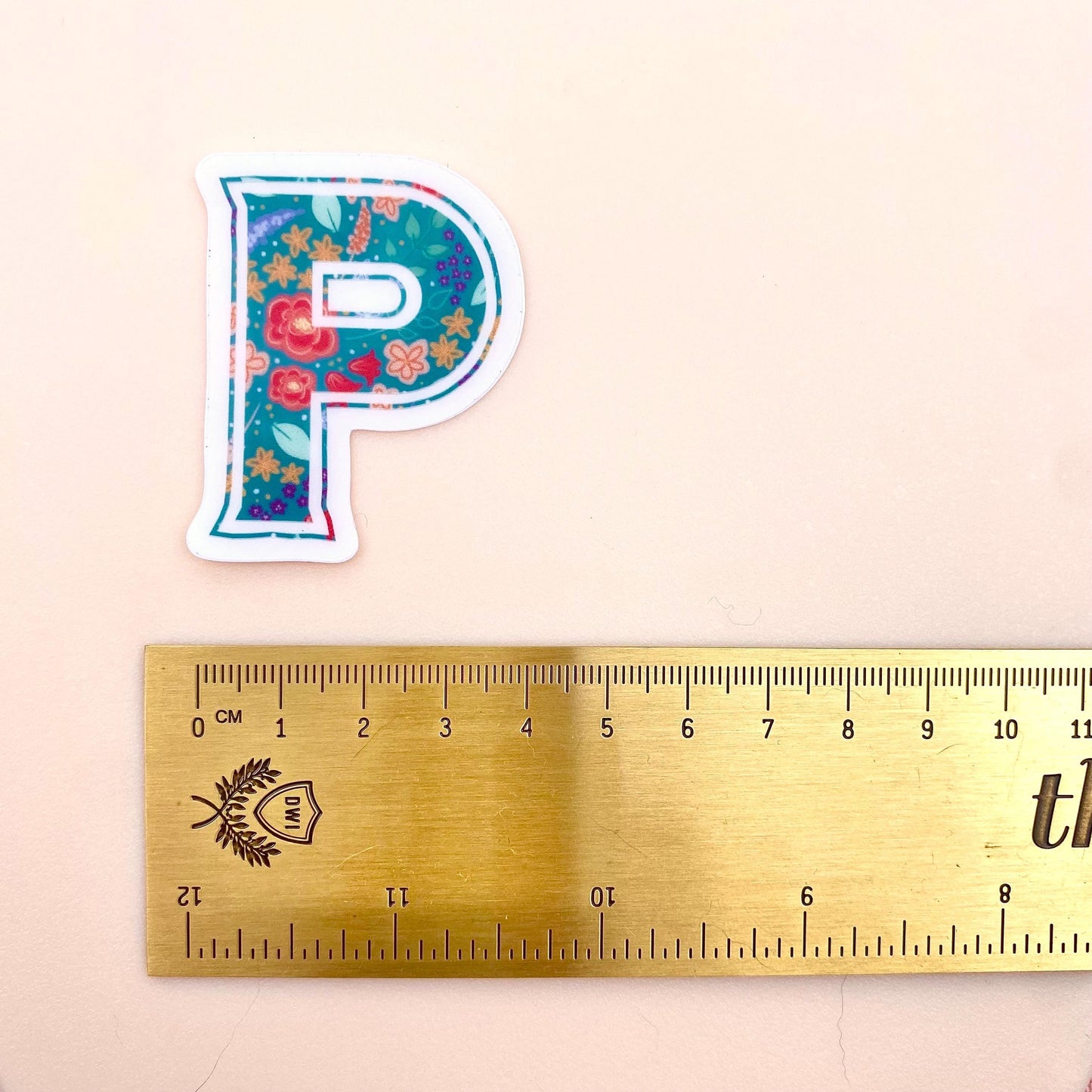 Decorative letter 'P' sticker with floral pattern on a white background with a gold ruler for scale.