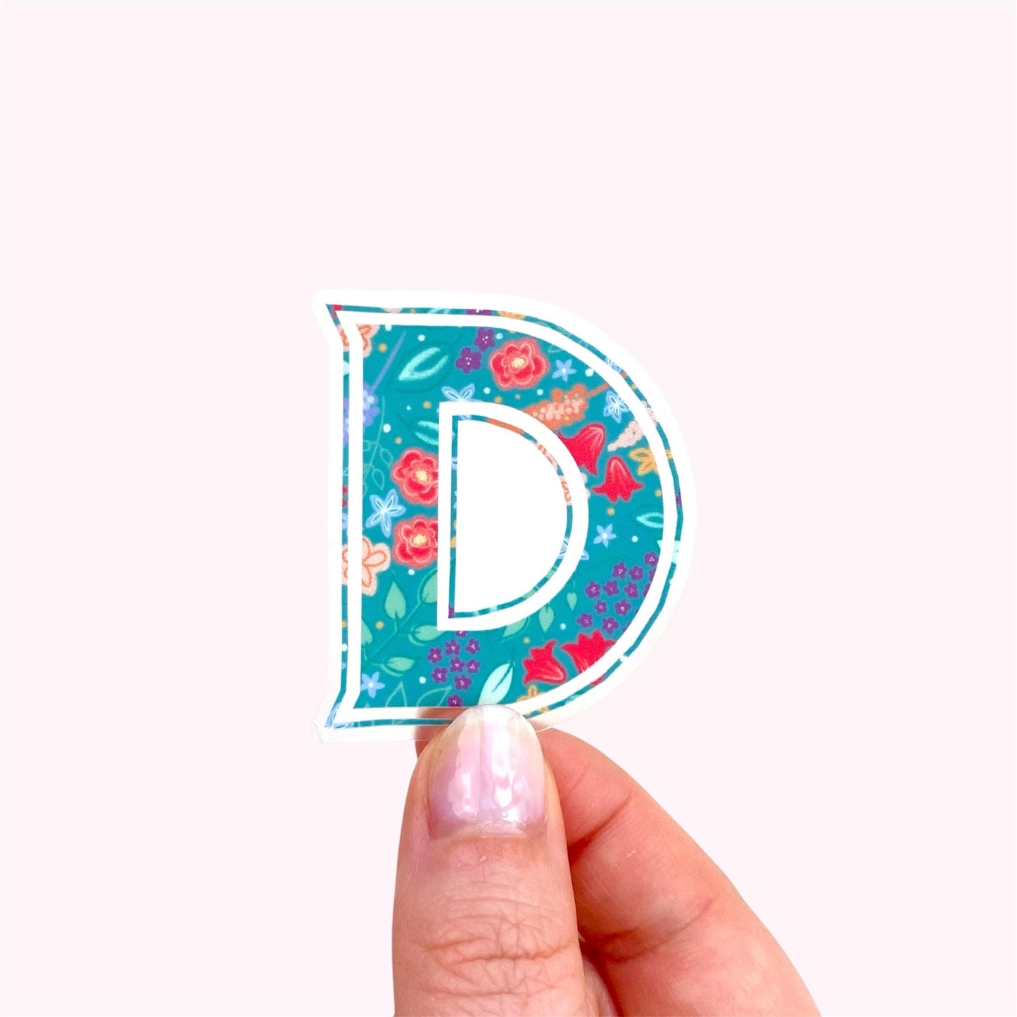Sticker with a floral design and letter 'D' held by a hand on a white background