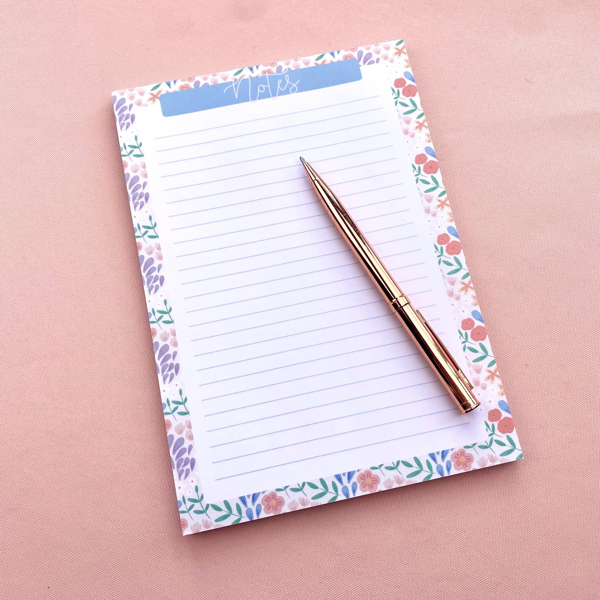 Floral notepad with a pen on a pink background